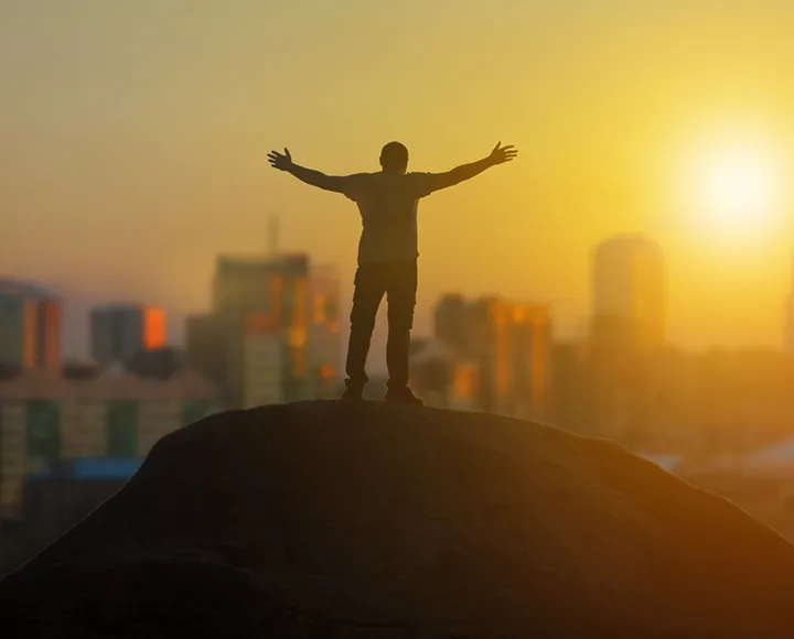 A man standing on a hill with his arms opening looking at the city skyline A man standing on a hill with his arms opening looking at the city skyline